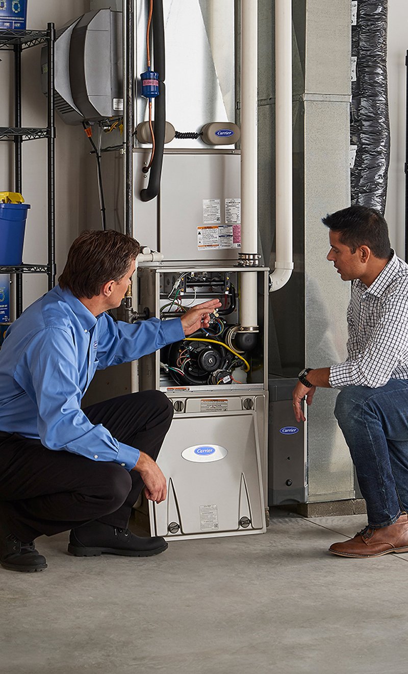 HVAC technician showing a homeowner the components of an open gas furnace.