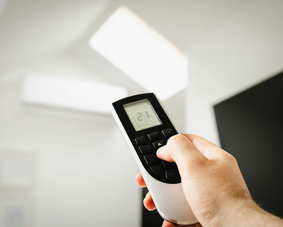 Hand adjusting an indoor cooling unit with a remote control set to 21 degrees