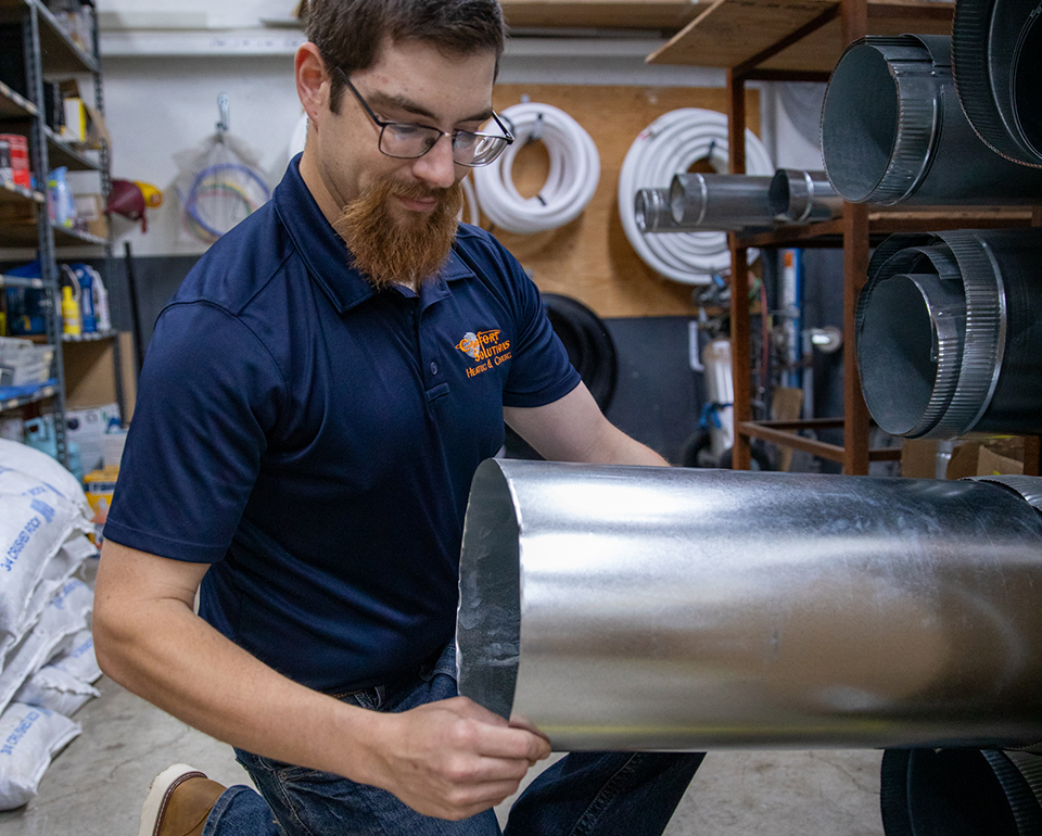 Comfort Solutions technician handling sheet metal ductwork in the fabrication shop