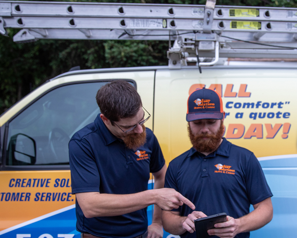 Two Comfort Solutions technicians reviewing a job on a tablet beside their service van