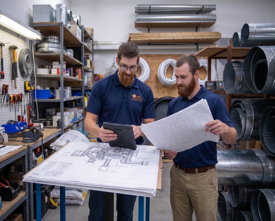 Two Comfort Solutions Heating & Cooling HVAC Technicians analyzing ductwork schematics inside an office