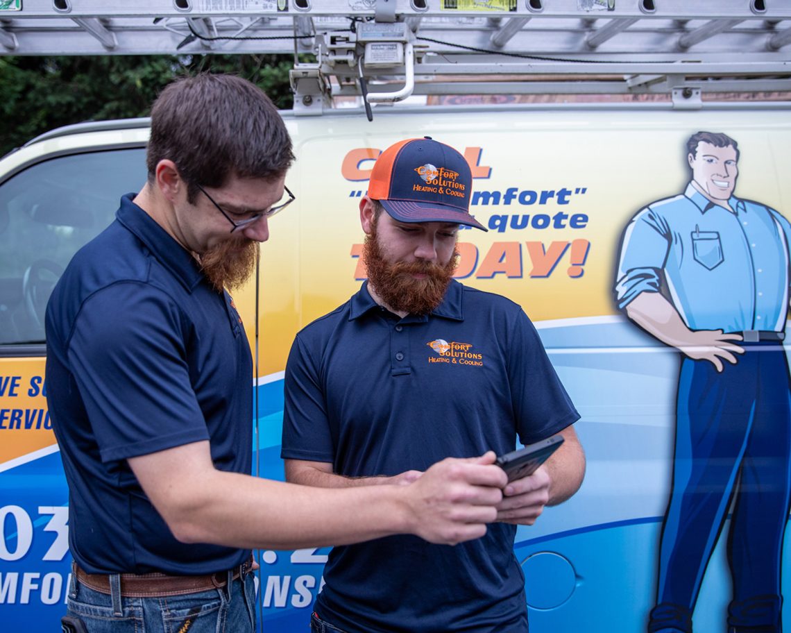 Comfort Solutions Heating & Cooling HVAC Technicians reviewing a project in front of their work van.