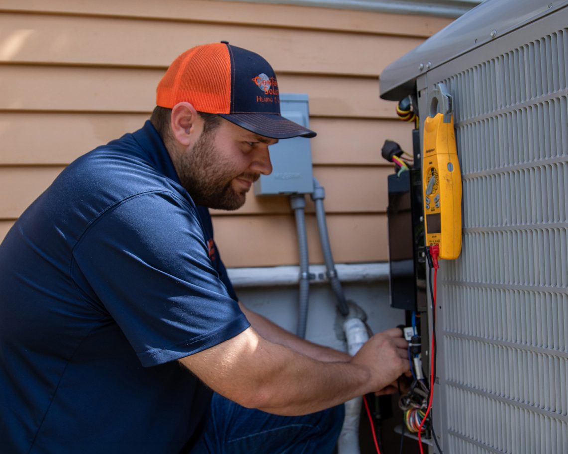 A comfort solutions HVAC technician working on a heat pump outside a home.